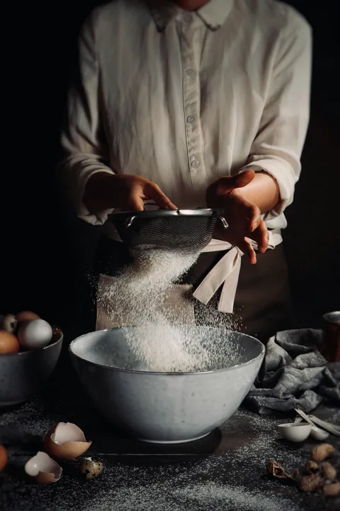 Hands sifting flour into a bowl